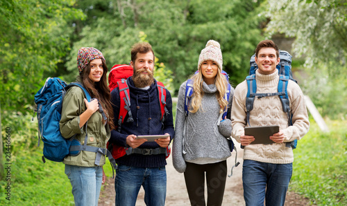 travel, technology and hiking concept - group of smiling friends or travelers with backpacks and tablet pc computers outdoors