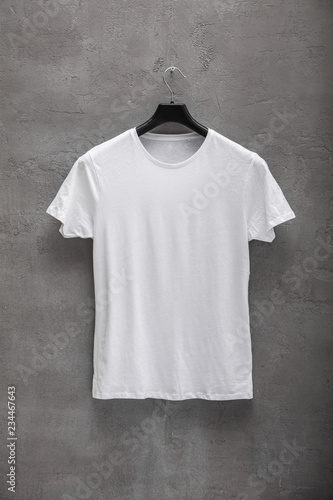 Front side of male white cotton t-shirt on a hanger and a concrete wall in the background. T-shirt without print