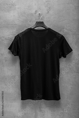 Back side of male black cotton t-shirt on a hanger and a concrete wall in the background. T-shirt without print