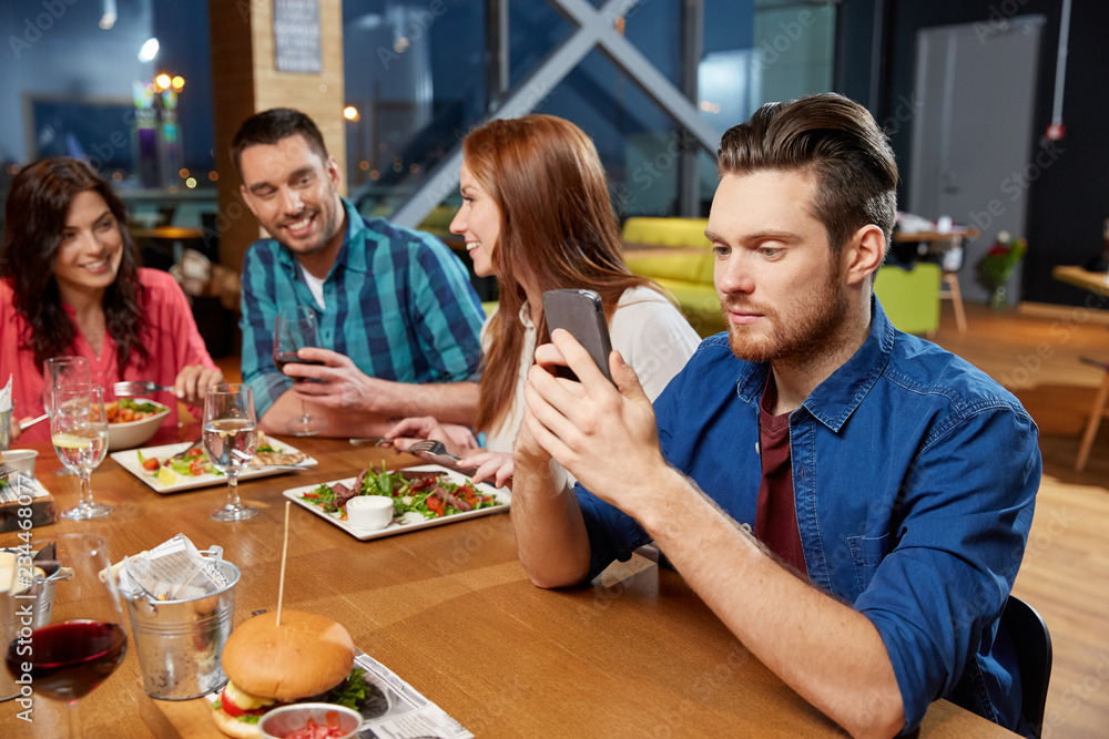 technology, lifestyle and people concept - man dining with friends and messaging on smartphone at restaurant