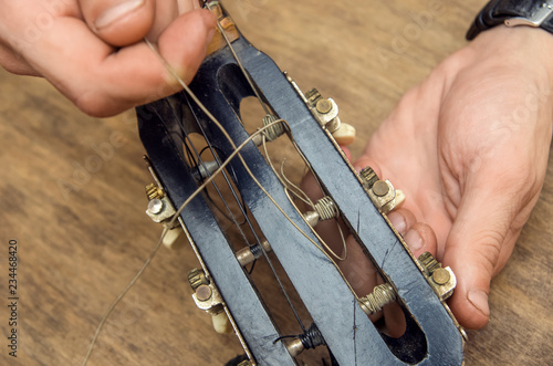 Lute maker shop and classical music instruments: young adult artisan fixing old classic guitar adding a cord and tuning the instrument. Close up of hands and palette photo