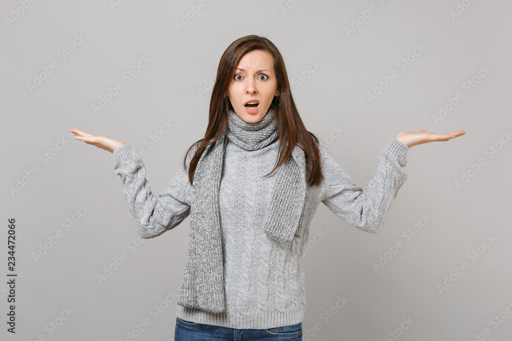 Perplexed young woman in gray sweater, scarf spreading, pointing hands aside isolated on grey background in studio. Healthy fashion lifestyle, people emotions, cold season concept. Mock up copy space. Perplexed young woman in gray sweater, scarf spreading, pointing hands aside isolated on grey background in studio. Healthy fashion lifestyle, people emotions, cold season concept. Mock up copy space.