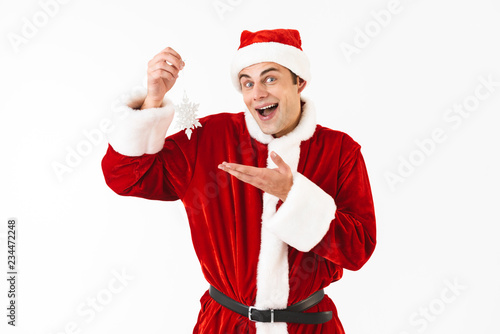 Image of joyful man 30s in santa claus costume holding paper snowflake, isolated on white background in studio