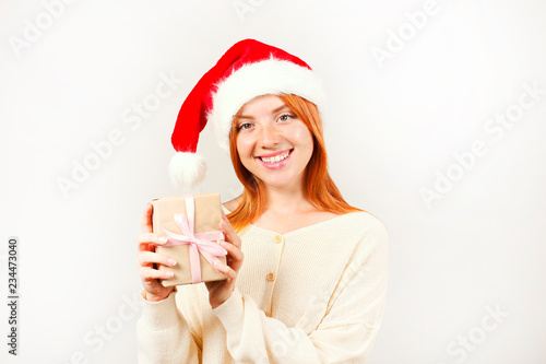 Close up portrait of beautiful redheaded young woman wearing Santa Claus hat   white sweater with satisfied facial expression. Cute female celebrating New Year. Copy space  isolated white background.