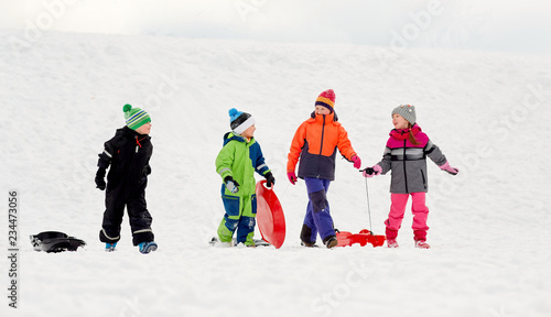 childhood, sledging and season concept - group of happy little kids with sleds outdoors in winter