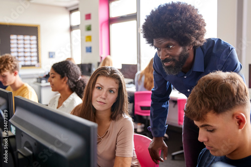 Male Teacher Helping Teenage Female High School Student Working In Computer Class