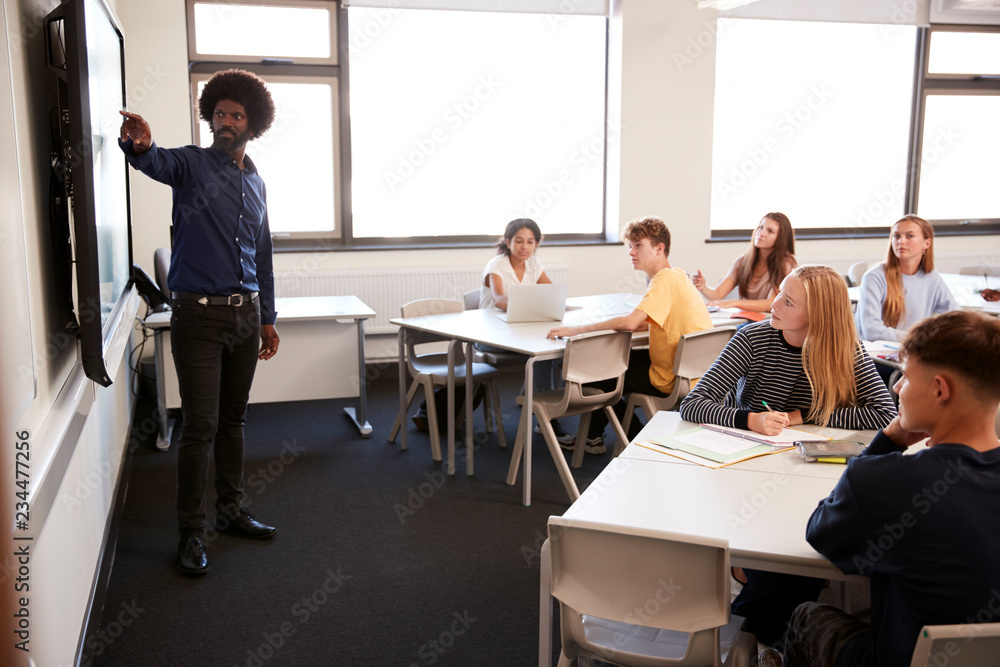 Male High School Teacher Standing Next To Interactive Whiteboard And Teaching Lesson Male High School Teacher Standing Next To Interactive Whiteboard And Teaching Lesson