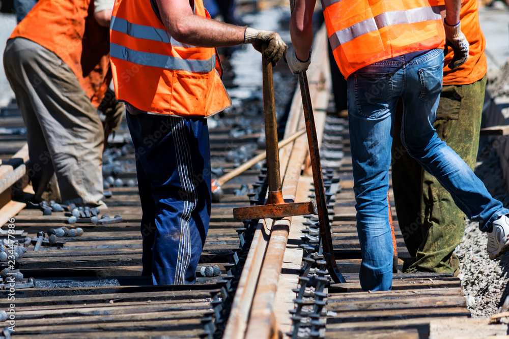 Workers in bright uniforms lay railway or tram tracks Workers in bright uniforms lay railway or tram tracks