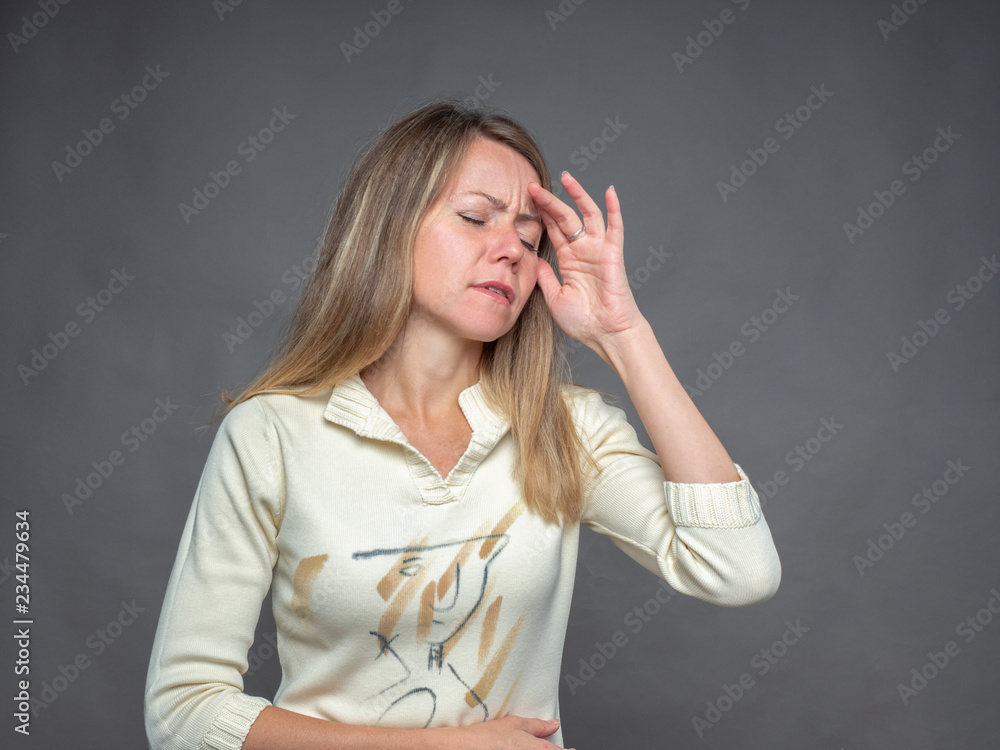 Emotional woman holding hand on forehead, suffering from pain feeling bad and sick. She Having headache and fever. Portrait isolated on gray background. Portrait of adult girl shooting in studio Emotional woman holding hand on forehead, suffering from pain feeling bad and sick. She Having headache and fever. Portrait isolated on gray background. Portrait of adult girl shooting in studio