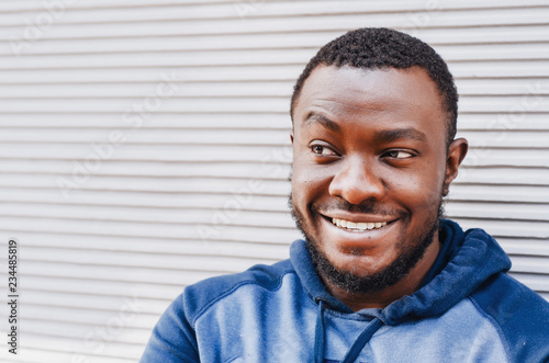 Portrait of a black guy close-up in a sports sweater on the background of a striped bright wall. Cheerful positive person. City photo, space. Youthful culture.