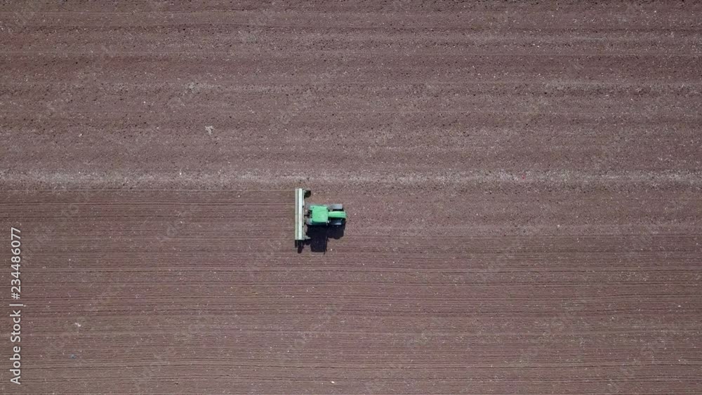 Green Tractor cultivating and seeding a dry field - Top down aerial footage. Green Tractor cultivating and seeding a dry field - Top down aerial footage.