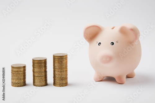 Close up of pink piggy money bank, stacks of golden coins isolated on white wall background. Money accumulation investment banking or business services, wealth concept. Copy space advertising mock up.