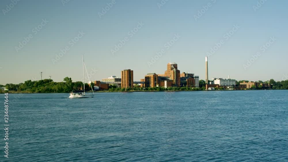 Sailboat Cruising Down River In Front Of Industrial Plant Sailboat Cruising Down River In Front Of Industrial Plant