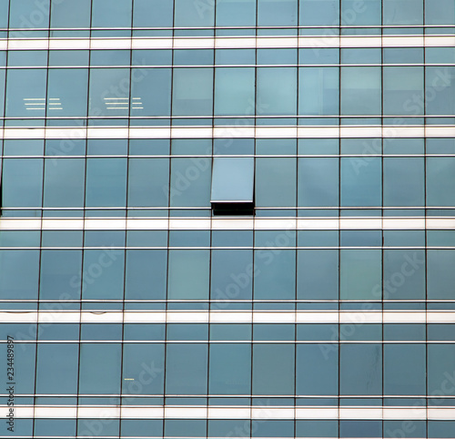 The glass facade of skyscraper with many identical windows and only one window is different. Same glasses structure of house wall with one exception - open window.