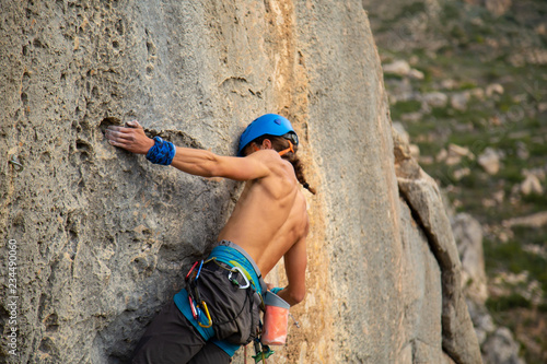 Shirtless climber man climbing mountain wall on amazing sunny day