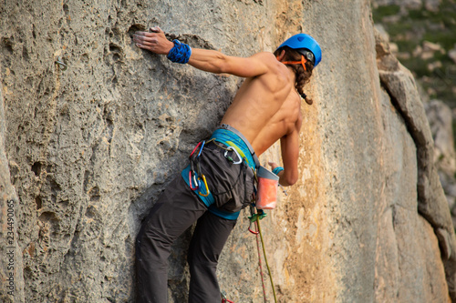 Shirtless climber man climbing mountain wall on amazing sunny day