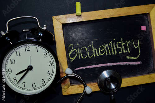 The words Biochemistry handwriting on chalkboard on top view. Alarm clock, stethoscope on black background. With education, medical and health concepts