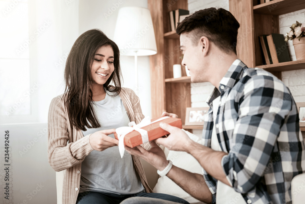 From me with love. Cheerful girl expressing positivity while looking at present in red paper From me with love. Cheerful girl expressing positivity while looking at present in red paper