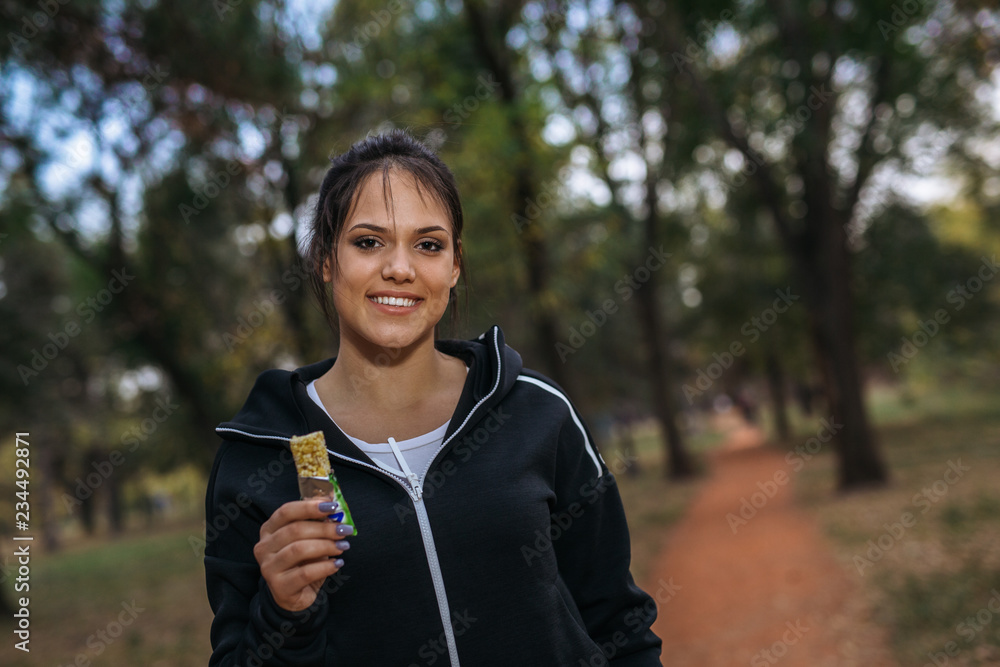 Portrait of beautiful woman preparing to exercise in park, holding granola bar Portrait of beautiful woman preparing to exercise in park, holding granola bar