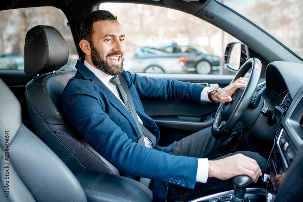 Handsome bearded businessman dressed in the suit driving a car in the city Handsome bearded businessman dressed in the suit driving a car in the city