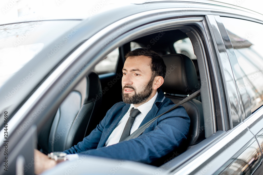 Handsome bearded businessman dressed in the suit driving a car in the city