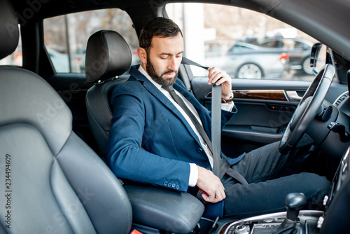 Elegant businessman dressed in the suit fastening the safe belt before driving his car