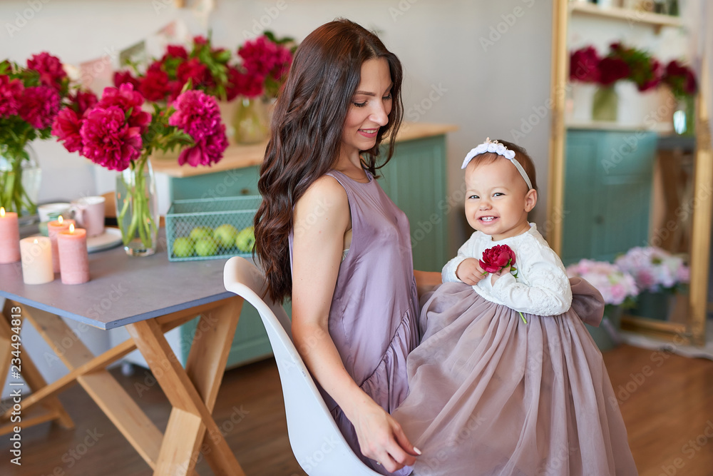 Family mother and daughter with peonies flowers in kitchen at home. Happy mother and baby daughter. Happy family. Greeting card for mother's day, for March 8, Women's Day. Birthday greetings template Family mother and daughter with peonies flowers in kitchen at home. Happy mother and baby daughter. Happy family. Greeting card for mother's day, for March 8, Women's Day. Birthday greetings template