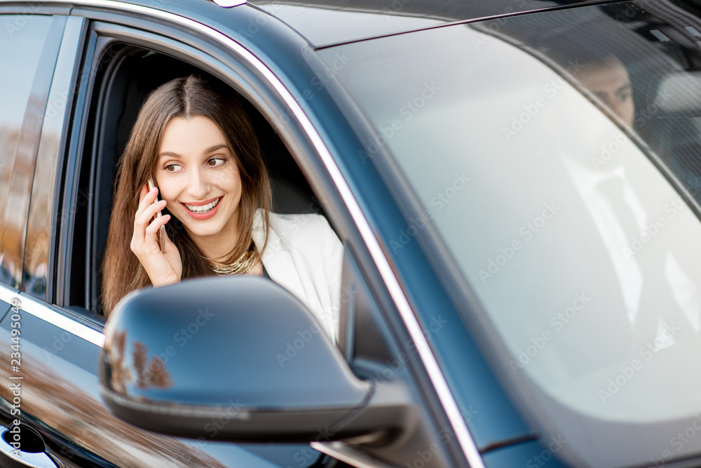 Elegant businesswoman talking with phone driving luxury car with businessman in the city, view from the outside through the window Elegant businesswoman talking with phone driving luxury car with businessman in the city, view from the outside through the window