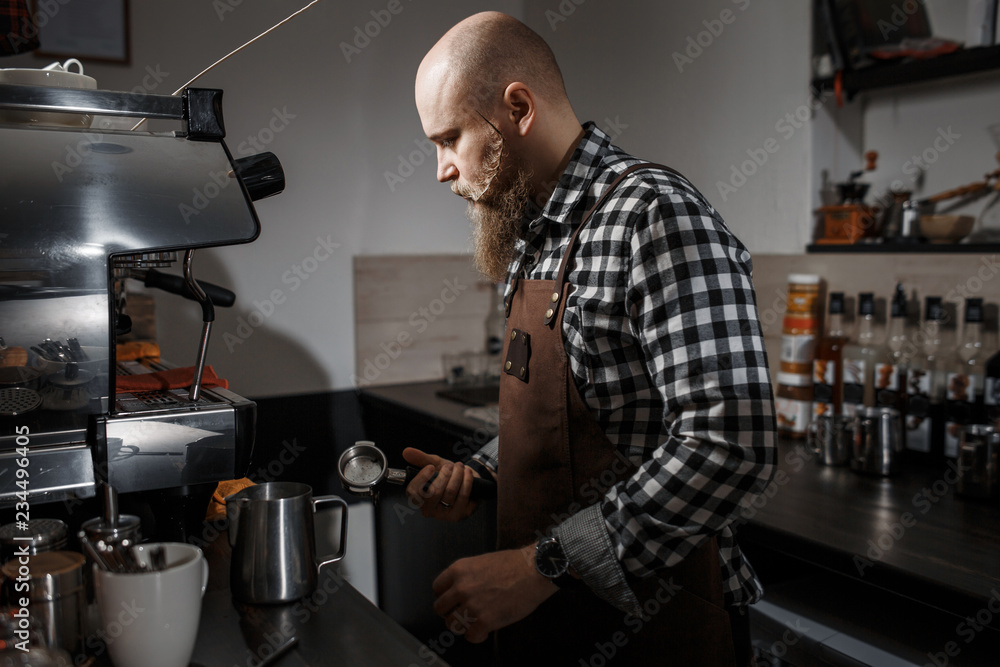 Brutal young barista in an apron makes coffee at the bar in a modern cafe Brutal young barista in an apron makes coffee at the bar in a modern cafe