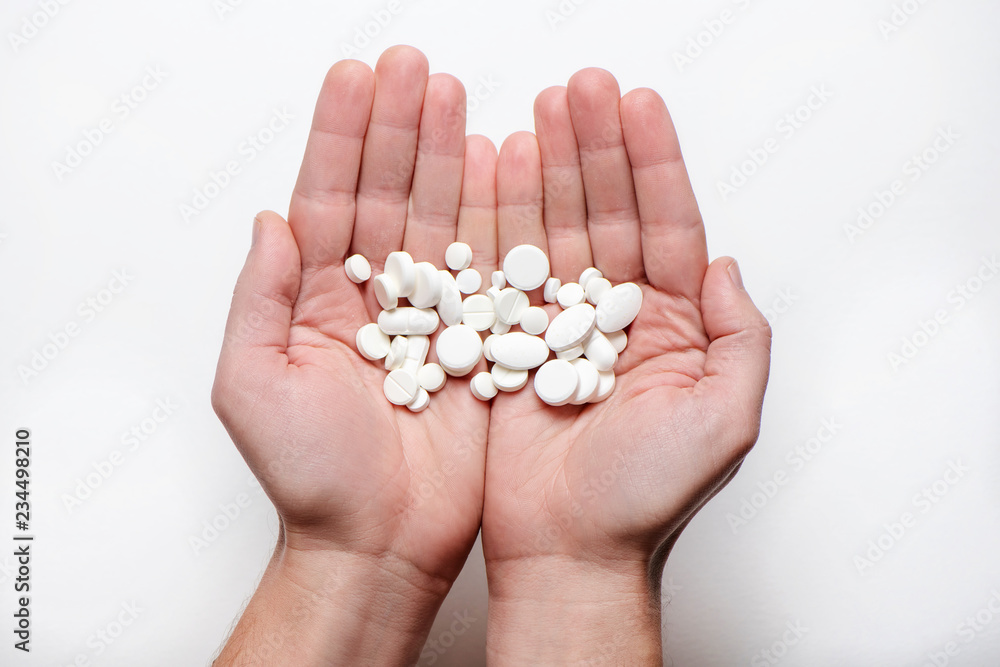 Handful of white pills in open palms on white background
