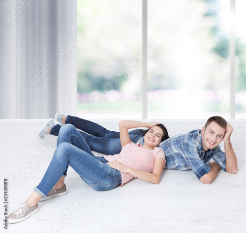 Happy young couple, lying on the floor, look at each other and dream of furniture for new apartment. Mock up for design.