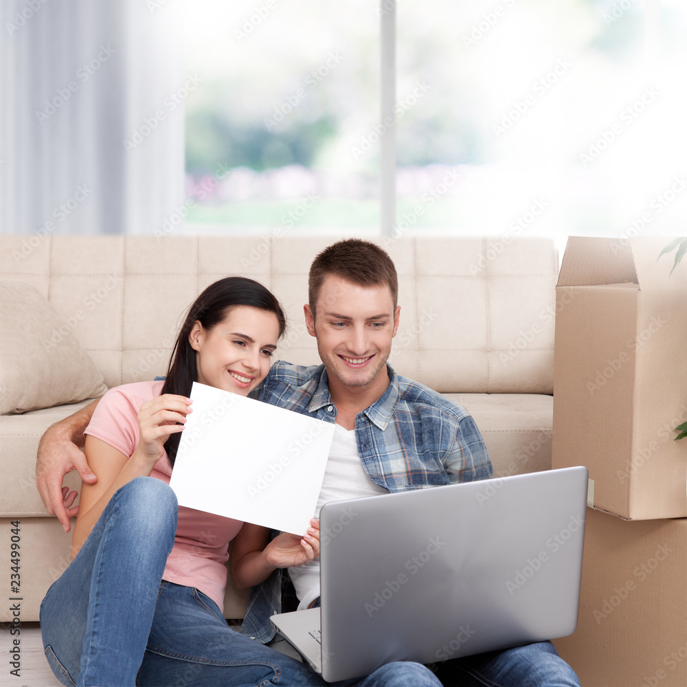 Beautiful young couple using laptop communicates. The woman smiles and shows a blank sheet of paper. Beautiful young couple using laptop communicates. The woman smiles and shows a blank sheet of paper.