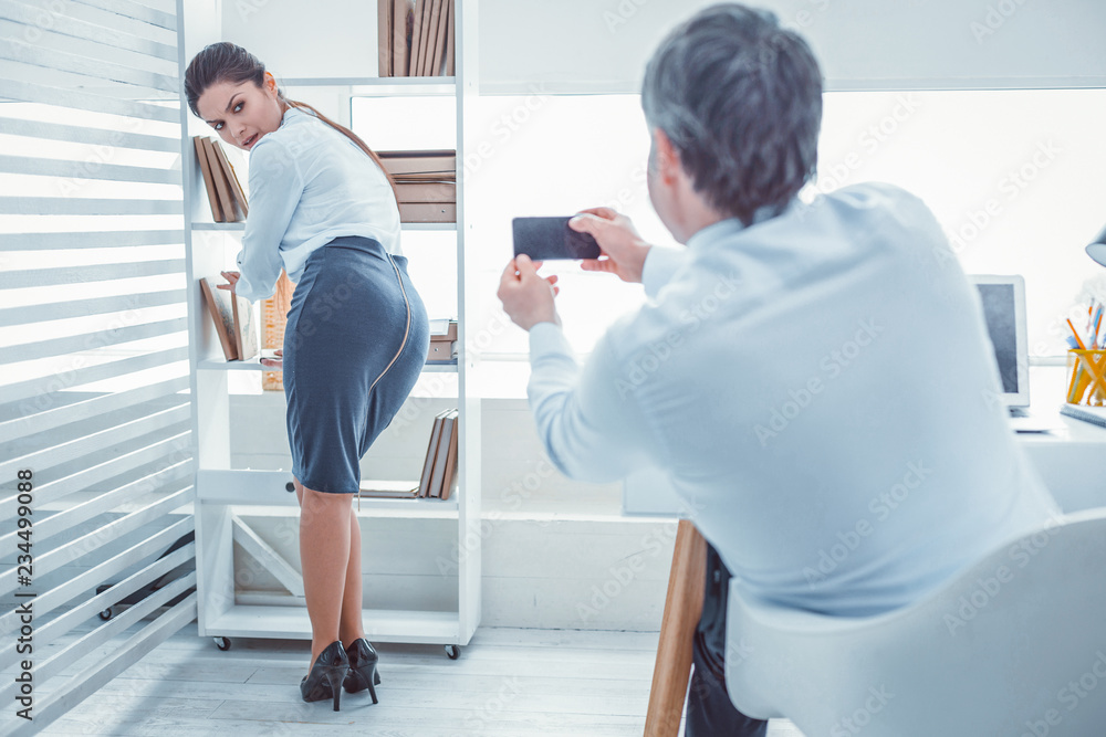 Fototapeta premium Boss making photos. Young confused woman feeling awfully because of her superior who secretly making photos