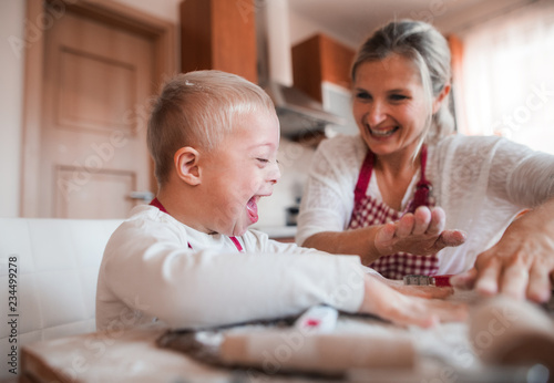 A laughing handicapped down syndrome child with his mother indoors baking. photo