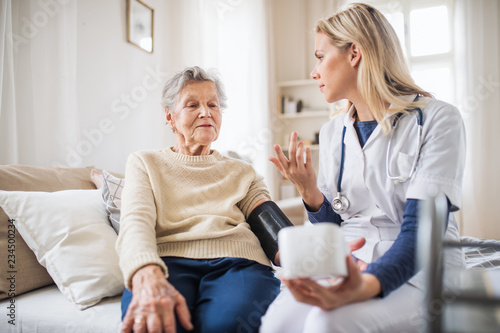 A health visitor measuring a blood pressure of a senior woman at home.