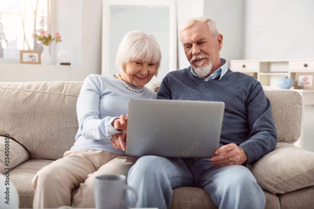 Happy moments. Senior couple having good time while watching pictures in the social media