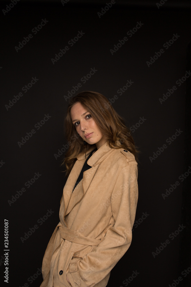 Portrait of young woman in black top and beige trench coat on black background Portrait of young woman in black top and beige trench coat on black background