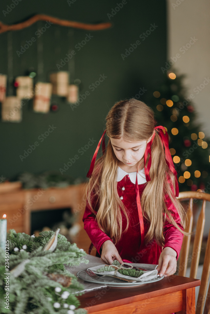 girl burgundy dress decorates Christmas rustic room