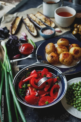 Delicious dinner table for two with fried potatoes  organic tomatoes salad  olives  green onion  eggplants  eggs on dark stone background.