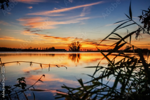 Sunset above lake in polder landscape with reflection in the water