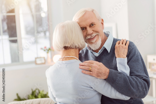 Elegant aging lady smiling while hugging her bearded husband
