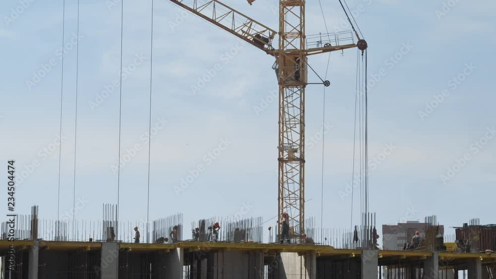 Builders on Unfinished Residential Building Construction Site in modern city landscape. Aerial shot. Multi-storey appartment house In The Course Of development. Yellow Tower Building Crane Builders on Unfinished Residential Building Construction Site in modern city landscape. Aerial shot. Multi-storey appartment house In The Course Of development. Yellow Tower Building Crane