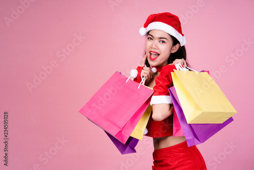 Beautiful Asian women wearing bright red santa claus carrying colorful shopping bags. On pink background. Christmas shopping And happy new year There are many discounts many stores around the world.