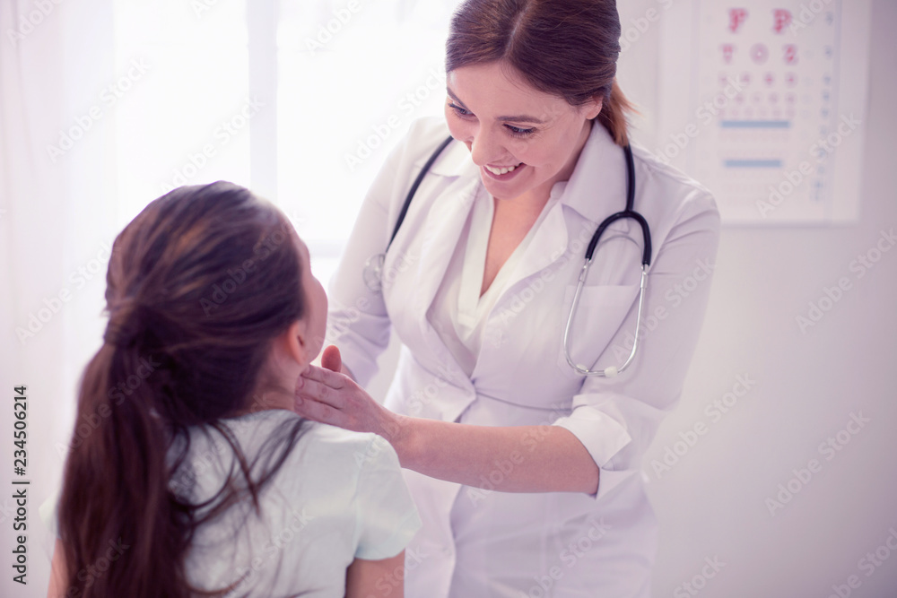 Smiling physician. Smiling caring family physician wearing white jacket exploring throat of little girl Smiling physician. Smiling caring family physician wearing white jacket exploring throat of little girl