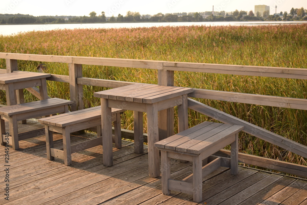Wooden tables and benches on the lake with reeds waiting for lovers to watch the sunset.