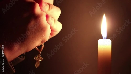 Man clasping hands with cross, praying near a burning candle