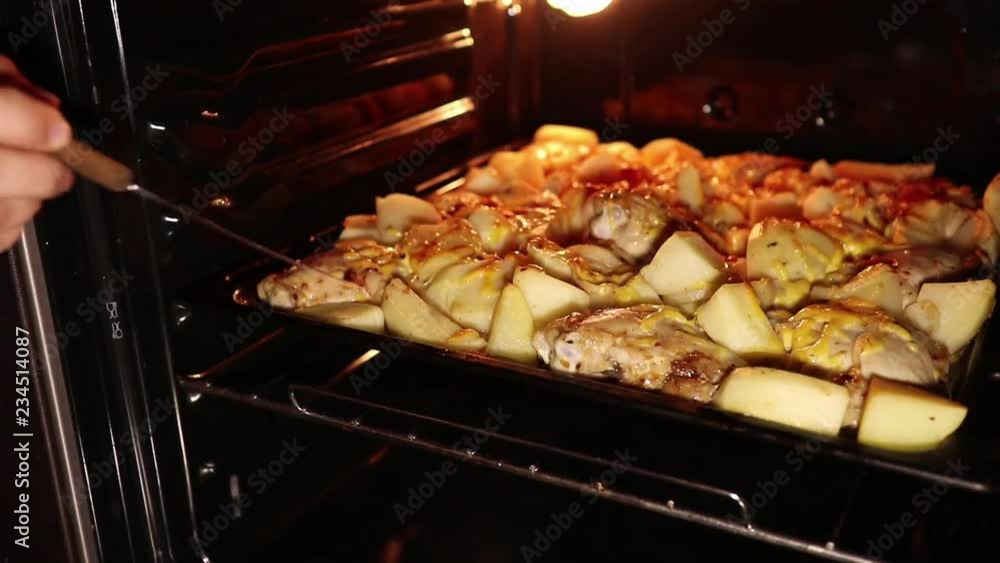 female hand checks cooking potatoes with chicken in the oven female hand checks cooking potatoes with chicken in the oven