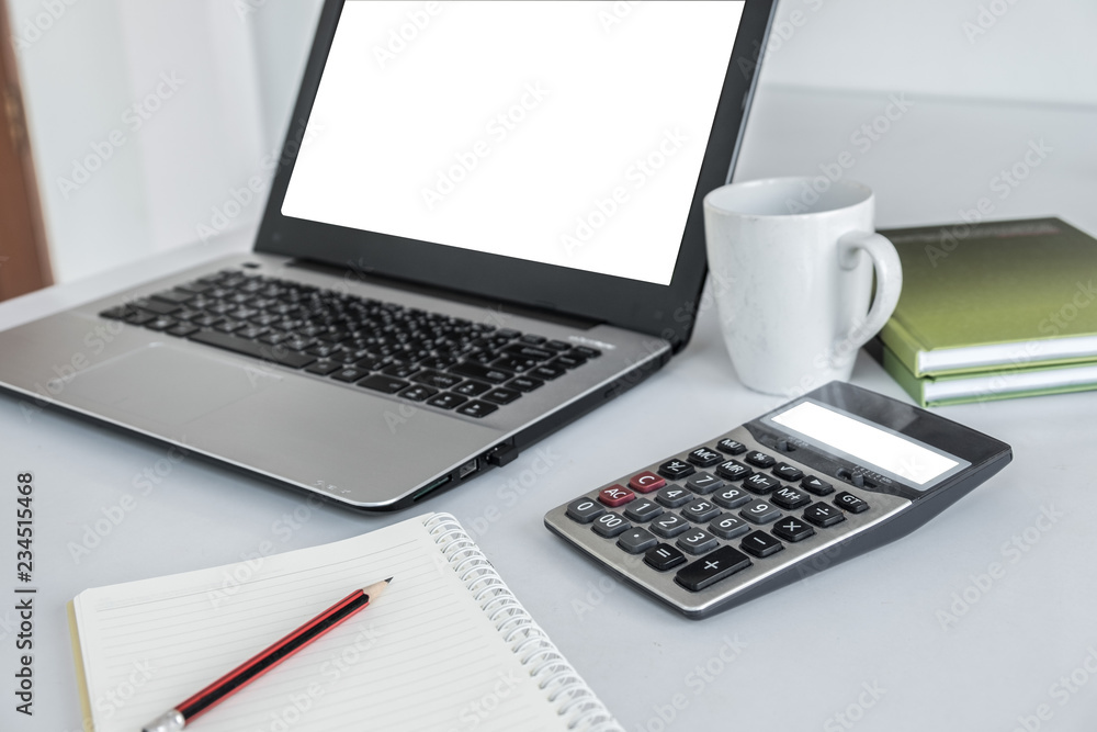 Laptop white screen ,calculator white screen ,white coffee mug, green book and a pencil placed over notebook. All on the white desk Laptop white screen ,calculator white screen ,white coffee mug, green book and a pencil placed over notebook. All on the white desk