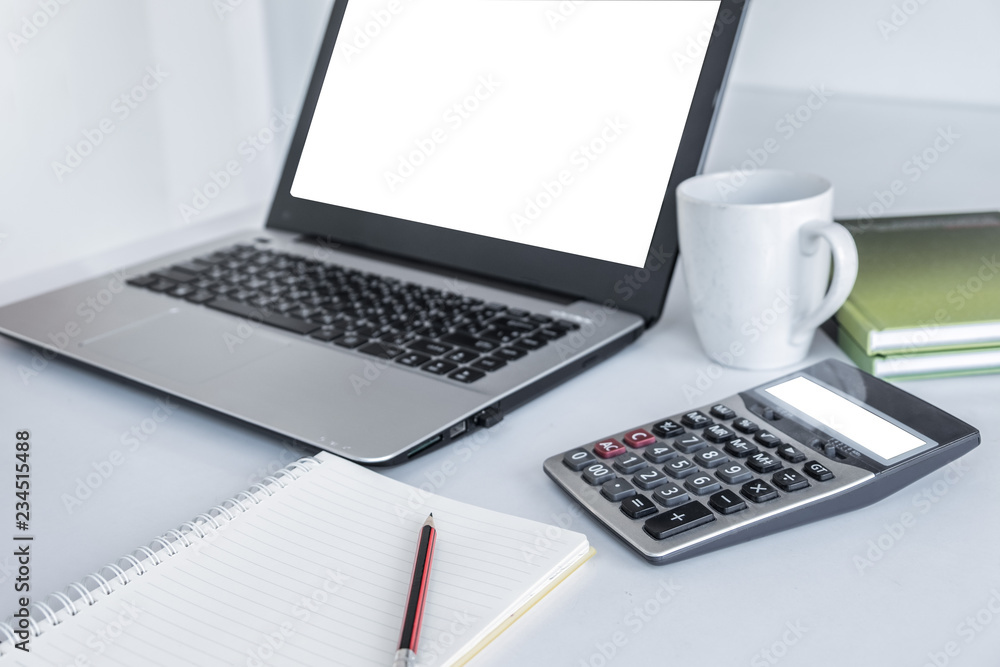 Laptop white screen ,calculator white screen ,white coffee mug, green book and a pencil placed over notebook. All on the white desk Laptop white screen ,calculator white screen ,white coffee mug, green book and a pencil placed over notebook. All on the white desk