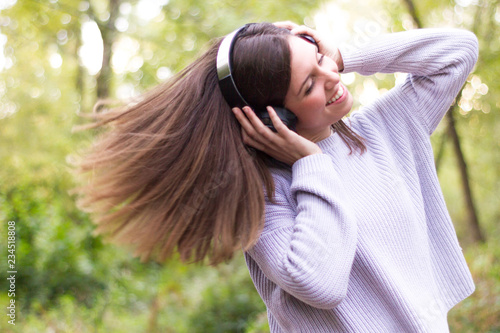 Caucasian european young woman or girl listening to music with helmets energetically and dancing moving her hair with energy in nature or very happy forest enjoying